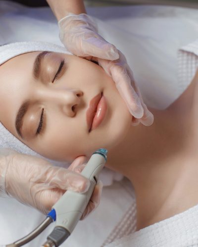 Side view of woman receiving microdermabrasion therapy on forehead at beauty spa. Hydrafacial procedure in Cosmetology clinic.